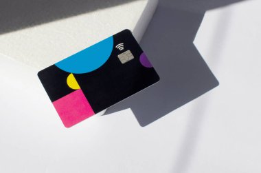 Yumuşak ışıklar ve gölgeli bir masanın üstünde görünen çipli plastik bir kredi kartı. Beyaz yüzeyde renkli kart. Konsept: finans, satın almalar, ödemeler, kredi, harcama, yatırım ve borçlar.