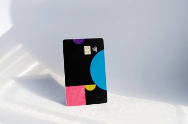 Yumuşak ışıklar ve gölgeli bir masanın üstünde görünen çipli plastik bir kredi kartı. Beyaz yüzeyde renkli kart. Konsept: finans, satın almalar, ödemeler, kredi, harcama, yatırım ve borçlar.