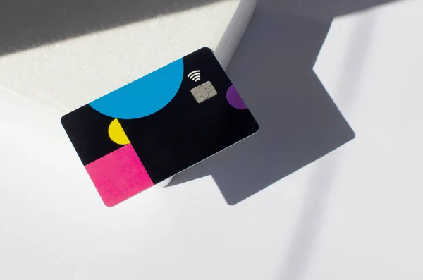 Plastic credit card with chip visible, on top of a table with soft lights and shadows. Colored card on white surface. Concept: finance, purchases, payments, loan, spending, investments and debts.