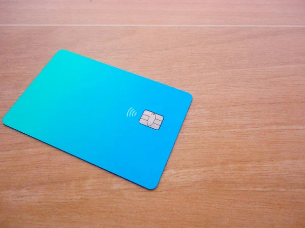 Plastic credit card with chip visible, on top of a table with soft lights and shadows. Blue card on wooden surface. Concept: finance, purchases, payments, loan, spending, investments and debts.