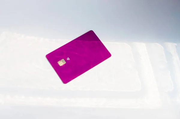 Plastic credit card with chip visible, on top of a table with soft lights and shadows. Purple card on white surface. Concept: finance, purchases, payments, loan, spending, investments and debts.