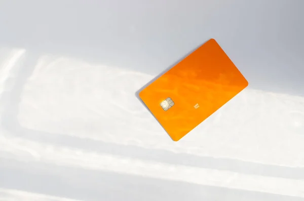 Yumuşak ışıklar ve gölgeli bir masanın üstünde görünen çipli plastik bir kredi kartı. Beyaz yüzeyde turuncu renkli kart. Konsept: finans, satın almalar, ödemeler, kredi, harcama, yatırım ve borçlar.