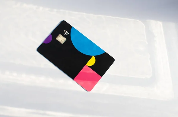 Plastic credit card with chip visible, on top of a table with soft lights and shadows. Colored card on white surface. Concept: finance, purchases, payments, loans, spending, investments and debts.