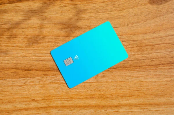 Plastic credit card with chip visible, on top of a table with soft lights and shadows. Blue card on wooden surface. Concept: finance, purchases, payments, loan, spending, investments and debts.