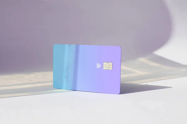Plastic credit card with chip visible, on top of a table with soft lights and shadows. Pink color card on white surface. Concept: finance, purchases, payments, loan, spending, investments and debts.
