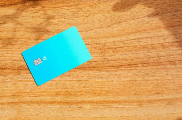 Plastic credit card with chip visible, on top of a table with soft lights and shadows. Blue card on wooden surface. Concept: finance, purchases, payments, loan, spending, investments and debts.