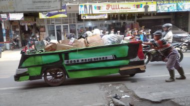 Bandung, Endonezya - 18 Temmuz 2022: İnsanlar tarafından atılan geri dönüşümlü bazı materyalleri el arabasında toplayarak geçinmek için çalışan ve sonra kullanılmış mal koleksiyoncularına satan bir adam..