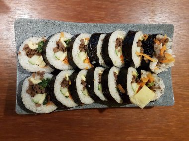 Gimbap, buharda pişirilmiş beyaz pirinç ve diğer çeşitli malzemelerden yapılan Kore yemeğidir. Tabakta..