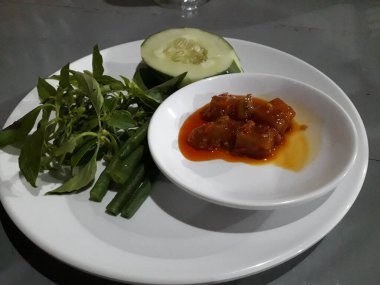 Kırmızı biber sosu ve beyaz tabakta çiğ sebze.