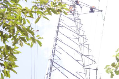 Banjarmasin, Güney Kalimantan, Endonezya - 10 Ağustos 2022: Elektrikçi yüksek voltaj tesislerinde yüksek voltaj kurulumu güvenli ve sistematik olarak bulanık doğal arka plan üzerinde.