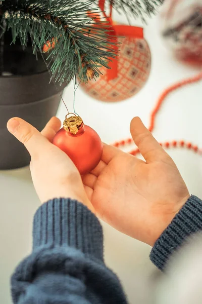 the hands of a boy in a Christmas sweater hold a Christmas tree decoration