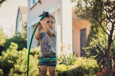 Happy child in nature. Happy childhood in the village. A child in the village, walking in the yard of a country house. The child is watering the lawn. Happy summer child.