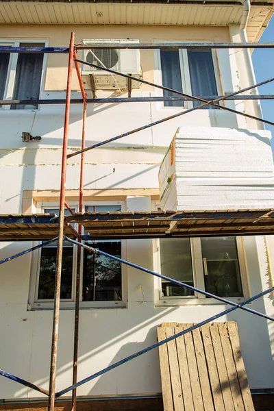 Modern repair and reconstruction of the house. Insulation of the house with polystyrene foam, plastering, applying plaster and painting facade walls using scaffolding when repairing the house. Construction or renovation.