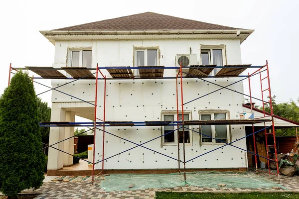 Modern repair and reconstruction of the house. Insulation of the house with polystyrene foam, plastering, applying plaster and painting facade walls using scaffolding when repairing the house. Construction or renovation.