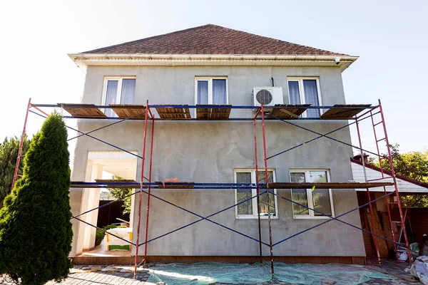 Modern repair and reconstruction of the house. Insulation of the house with polystyrene foam, plastering, applying plaster and painting facade walls using scaffolding when repairing the house. Construction or renovation.