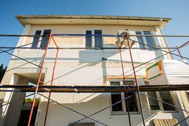 Modern repair and reconstruction of the house. Insulation of the house with polystyrene foam, plastering, applying plaster and painting facade walls using scaffolding when repairing the house. Construction or renovation.