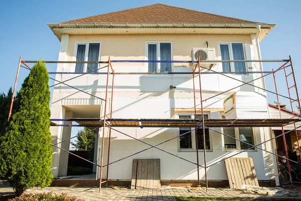 Modern repair and reconstruction of the house. Insulation of the house with polystyrene foam, plastering, applying plaster and painting facade walls using scaffolding when repairing the house. Construction or renovation.