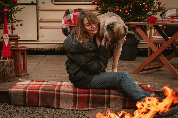 Happy young girl and dog spend time together on Christmas holidays. Cane Corso and his mistress celebrate the New Year in nature near the motor home and by the fire. New Year.