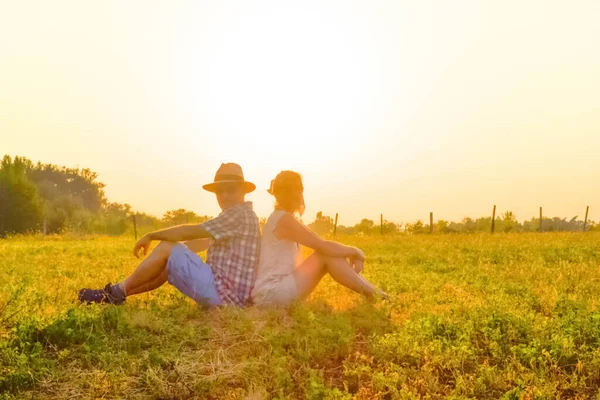 Portrait, in backlit, of a couple sitting in a meadow.