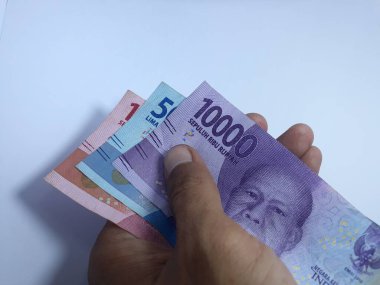 Rupiah 'a ait birkaç banknot, beyaz elin üzerinde izole bir şekilde duruyor. Rupiah Endonezya 'nın para birimidir.
