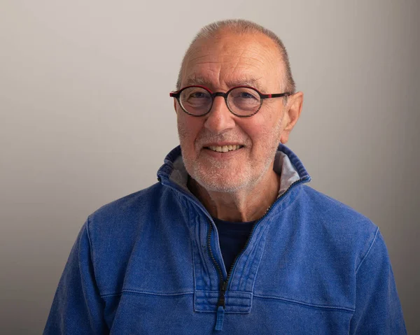 Portrait of a friendly smiling older man wearing glasses on a grey/gray background