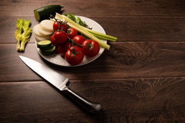 Salata malzemeleri ve bıçak. Koyu ahşap arka planda beyaz bir tabak. Kopya alanı var.