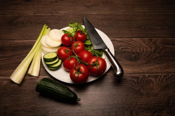 Salad ingredients and a knife a white plate on a dark wood background with copy space