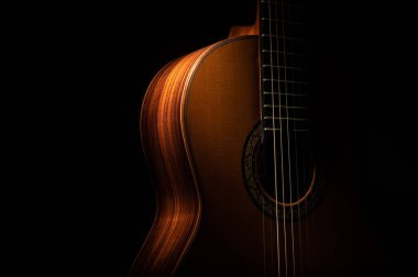 İspanyol klasik gitarı yakın çekimde, siyah bir arkaplanda, kopyalama alanı ile dramatik bir şekilde aydınlatılmış..  