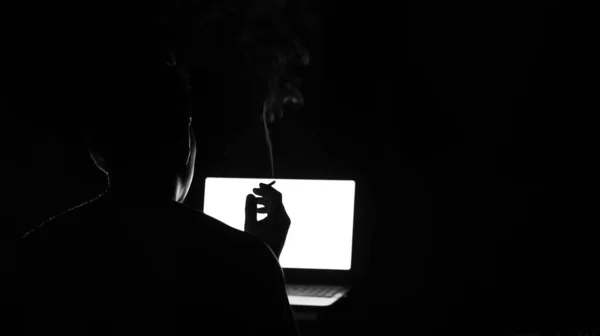 low key silhouette of male profile watching at laptop screen with blurry cigarettes smoke