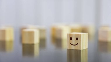 Happy face icon on wooden cube on black gloss wooden table. Background concept for happy and satisfied customer. Selected focus.