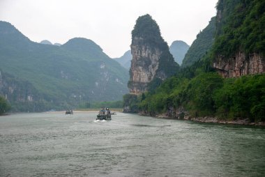 Zevkli gemiler Li Nehri boyunca hareket ediyor. Resimli dağların arkasına doğru.