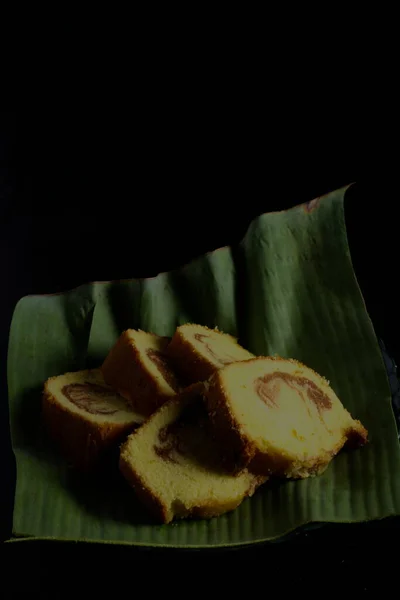 黒を背景にバナナの葉の容器に入ったケーキ — ストック写真