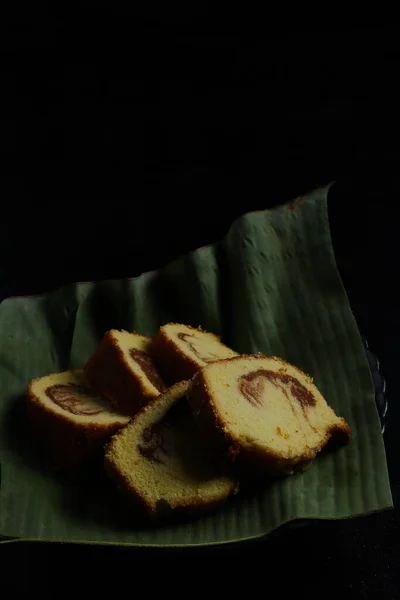 黒を背景にバナナの葉の容器に入ったケーキ — ストック写真