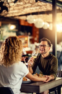 Young couple drinking wine and having fun during lunch in a bar. Focus is on man. 