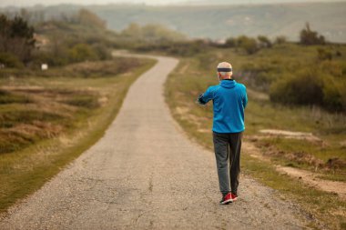 Back view of active mature sportsman taking a walk in nature in the morning. Copy space. 