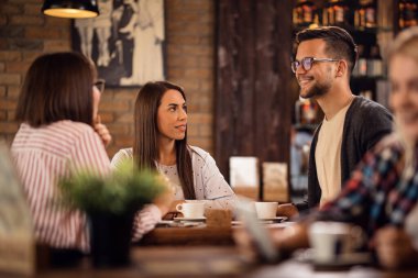 Group of friends drinking coffee and talking to each other in coffee shop. Focus is on a woman. 