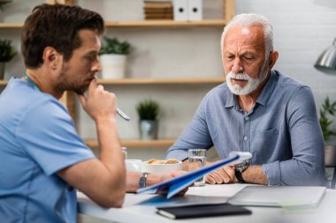 Senior man feeling worried while analzying his medical reports with a doctor during medical appointment.  