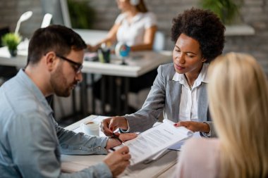 Black female real estate agent showing to a couple where to sign the contract during the meeting in the office. 