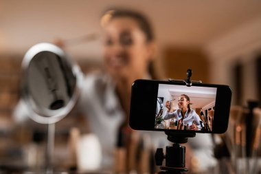Close-up of female influencer applying beauty products while filming make-up vlog.