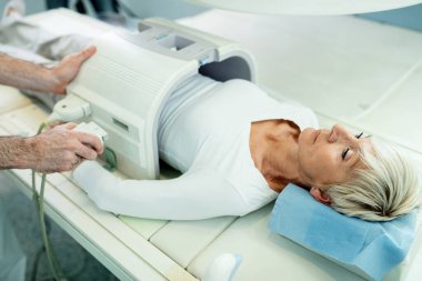 Mature woman being prepared for MRI scan of her abdomen by unrecognizable technician. 