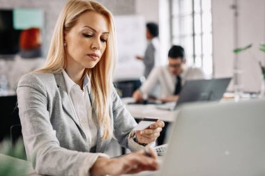 Businesswoman using credit card and computer for online shopping while being at work. 