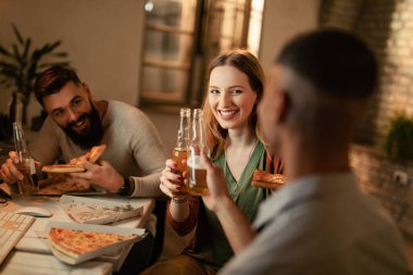Team of happy freelancers toasting with beer while eating pizza on a break in the office. 