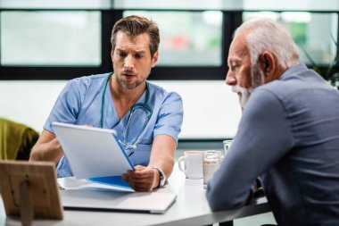 Serious doctor reading medical test results of his senior patient who came to medical appointment. 