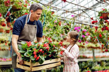 Male florist and his small daughter communicating while preparing crate with flowers for the market in a garden center. 