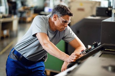 Male CNC machine operator working in factory plant.