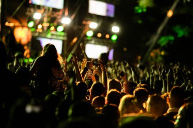 Back view of excited fans cheering at music concert and taking pictures with their smart phones. 