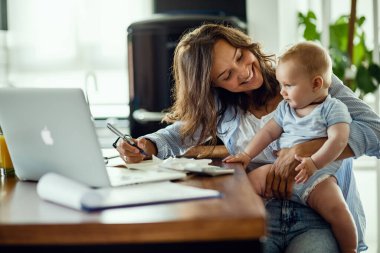 Young happy mother going through home finances and communicating with her baby son. 