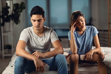 Young couple feeling frustrated after the argument and thinking of their relationship problems while sitting on the bed.