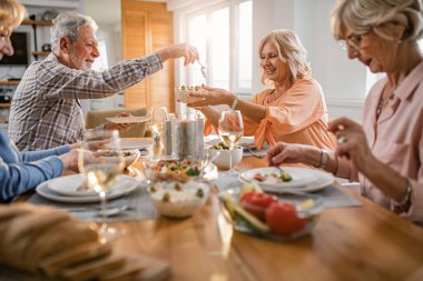 Happy mature people having lunch at dining table while woman is giving salad to her husband.