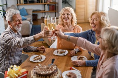Group of happy seniors toasting with champagne and having fun while celebrating birthday at home. 